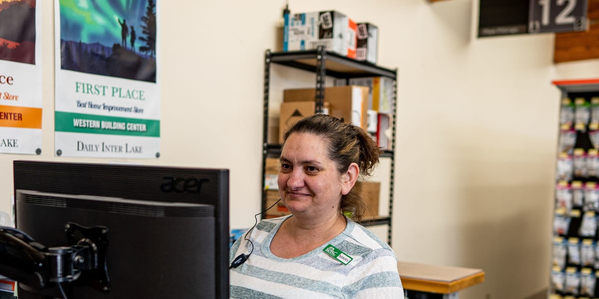 A female employee in a striped shirt with a Western Building Center name tag is working at the store's checkout counter, typi
