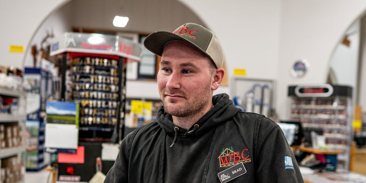 An employee wearing a black WBC (Western Building Center) hoodie and matching baseball cap stands behind the customer service