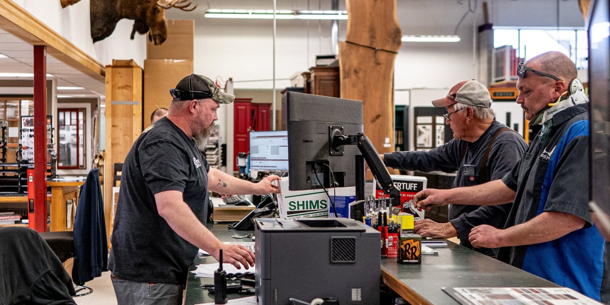 Three men are gathered around a workstation in what appears to be a customer service or workshop area of a Western Building C