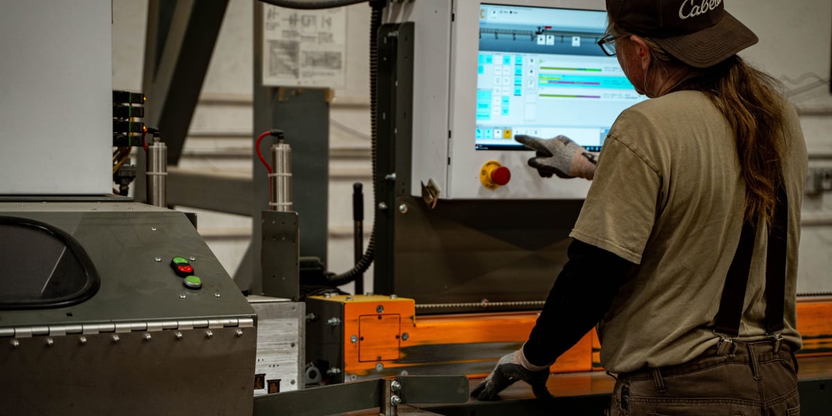 A female worker in work overalls and a cap operates industrial truss manufacturing equipment in a production facility