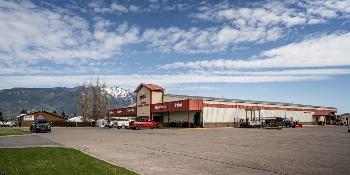 Exterior view of the Western Building Center Columbia Falls store, showing a large red and tan metal building with prominent