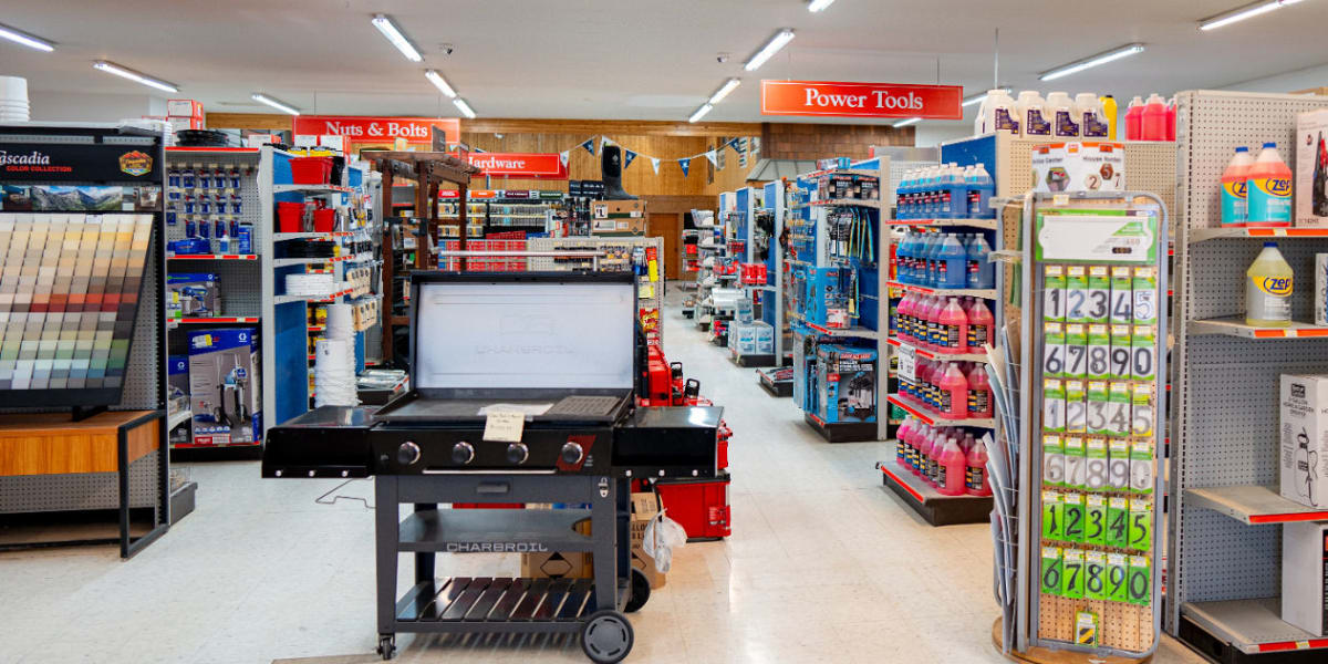 Interior view of a hardware store showing multiple aisles with organized shelving displaying various tools, hardware, and bui