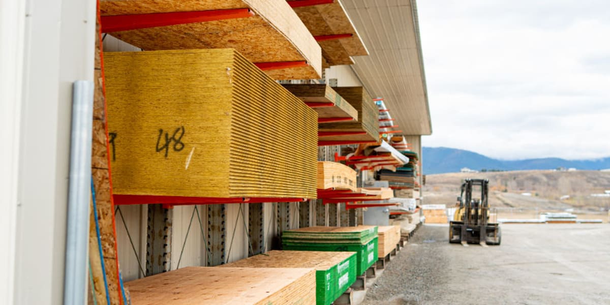 This image shows a covered lumber storage area at a building supply store, with stacks of dimensional lumber organized on can
