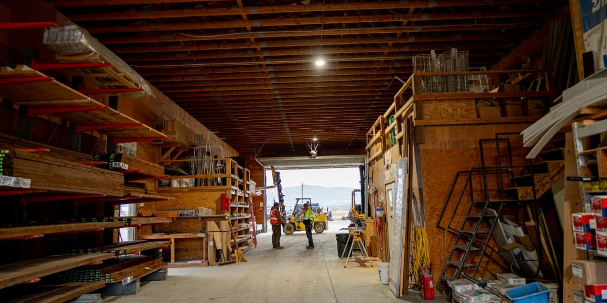 Interior view of a lumber warehouse showing exposed wooden ceiling joists and organized storage areas with lumber racks along
