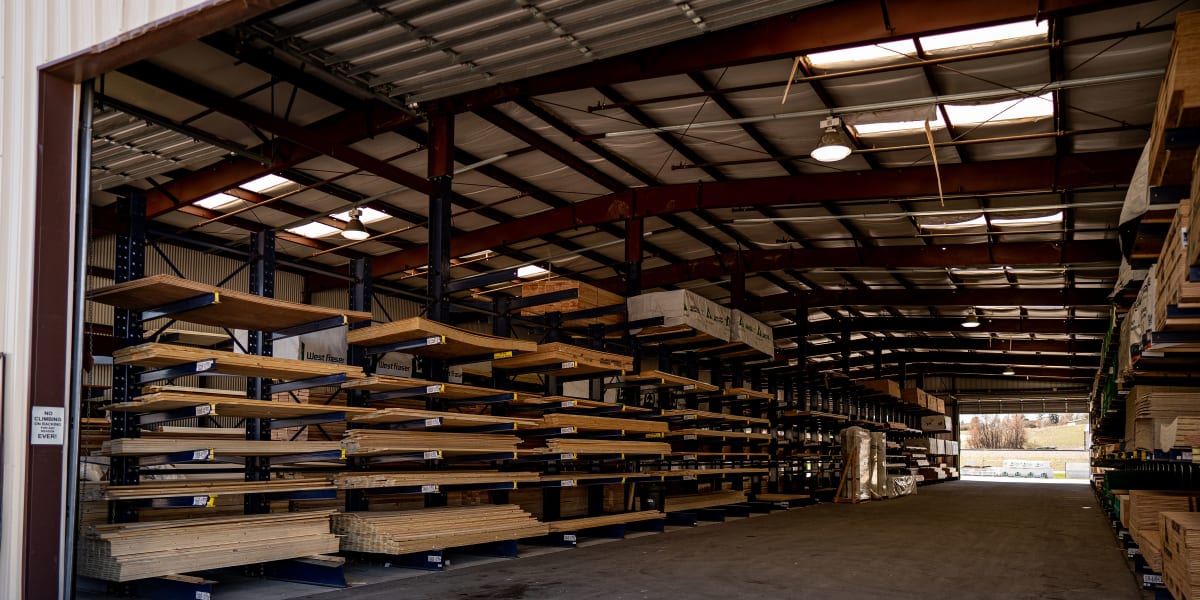 Interior view of a lumber warehouse showing extensive cantilever racking systems loaded with dimensional lumber, engineered l