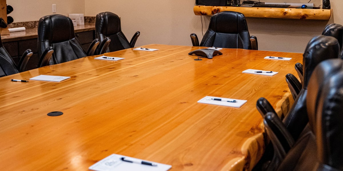 A professional conference room or meeting space with a large wooden conference table surrounded by black leather office chair