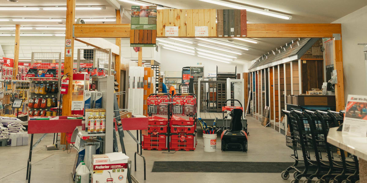 Interior view of a hardware store showing the main entrance area with fluorescent lighting and exposed beam ceiling