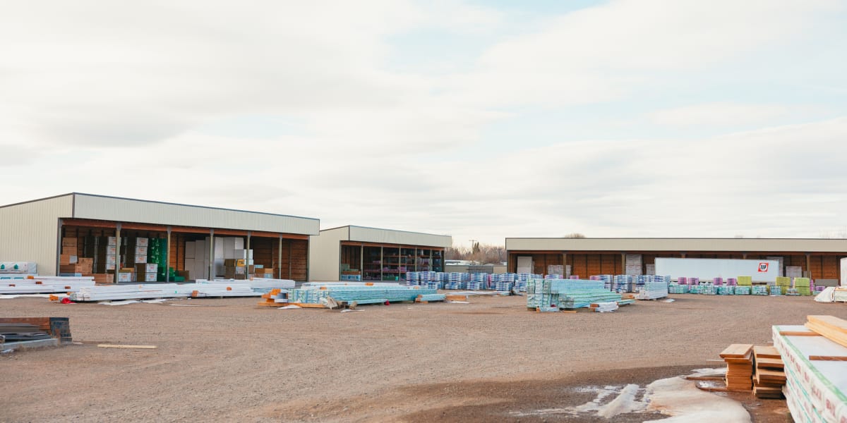 A wide view of a building supply lumber yard showing multiple warehouse buildings with metal roofing and wood-sided facades