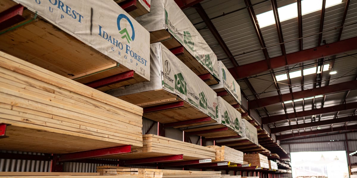 Interior view of a lumber warehouse showing organized stacks of dimensional lumber on red cantilever racking systems