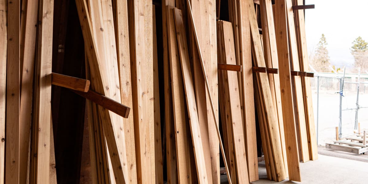 Interior view of a lumber storage warehouse showing numerous wooden boards and dimensional lumber pieces leaning against vert