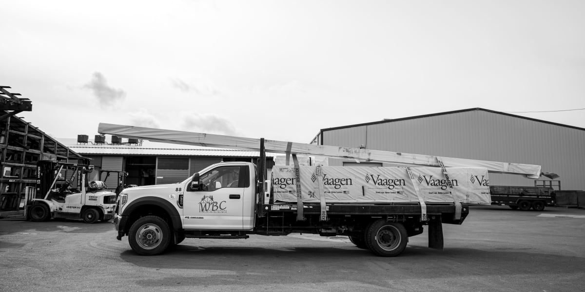 A black and white photograph showing a WBC (Western Building Center) delivery truck loaded with Vaagen brand lumber or buildi