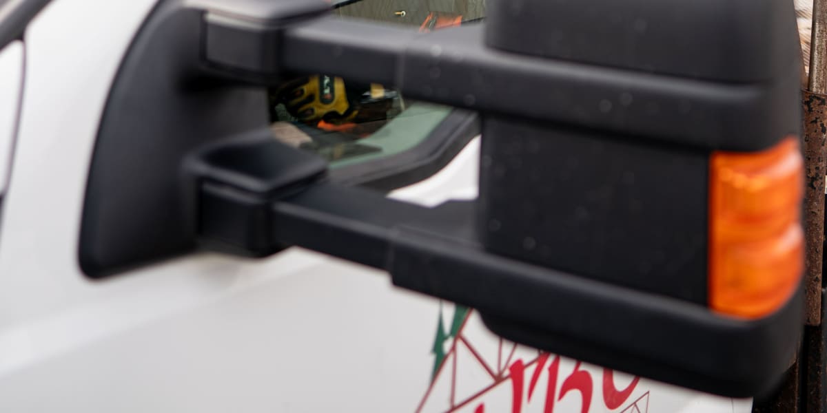 Close-up view of a white commercial work truck with amber warning lights on the roof and a metal mesh barrier or cage visible
