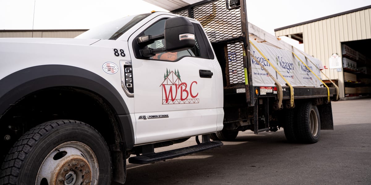 A white WBC (Western Building Center) delivery truck numbered 88 is parked in front of warehouse buildings at the lumber yard