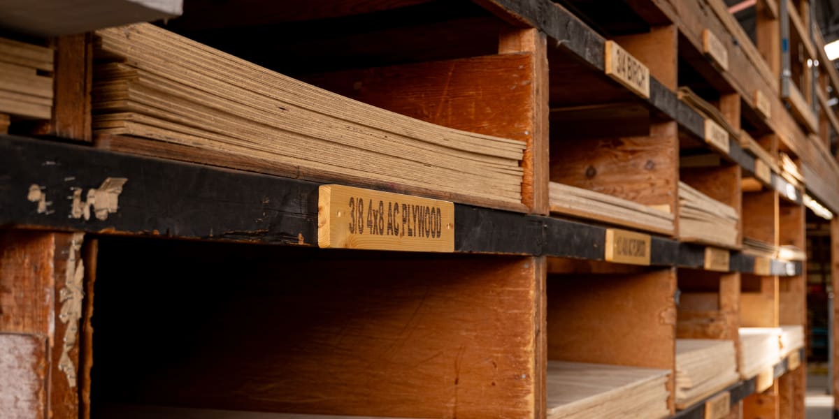 Interior view of a lumber warehouse showing organized wooden shelving units containing stacks of plywood and sheet materials