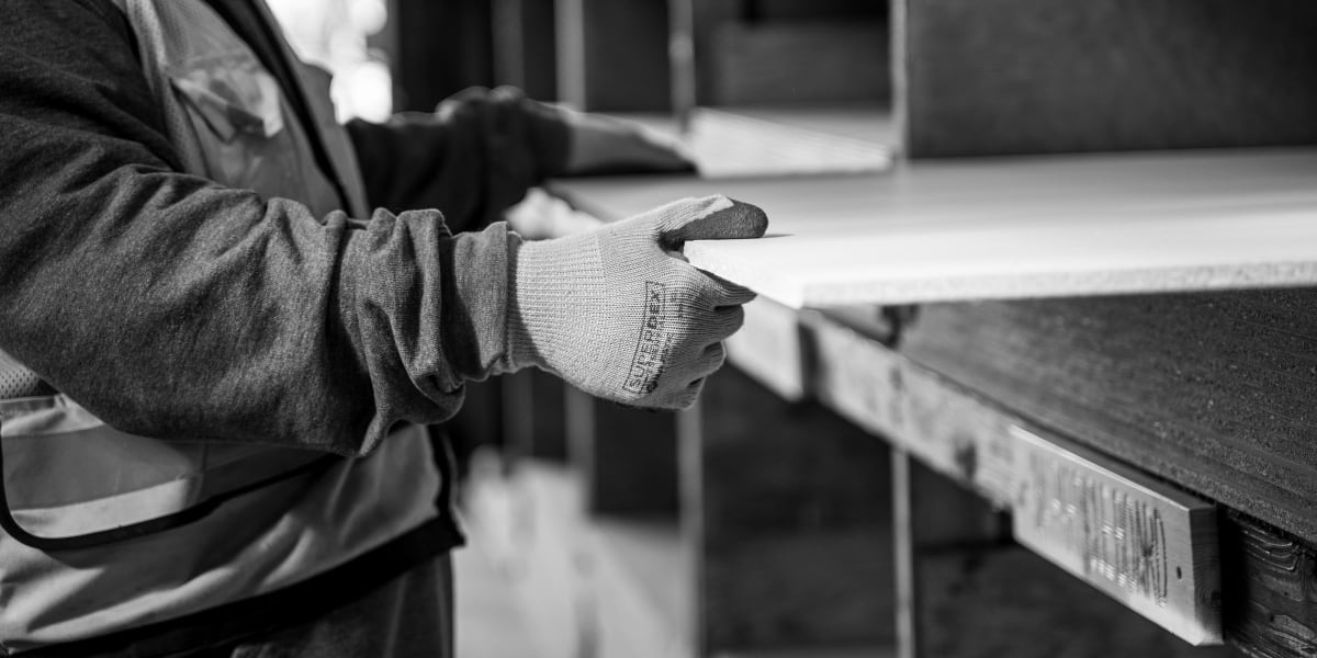 A black and white photograph showing a person in work gloves examining or handling dimensional lumber in what appears to be a