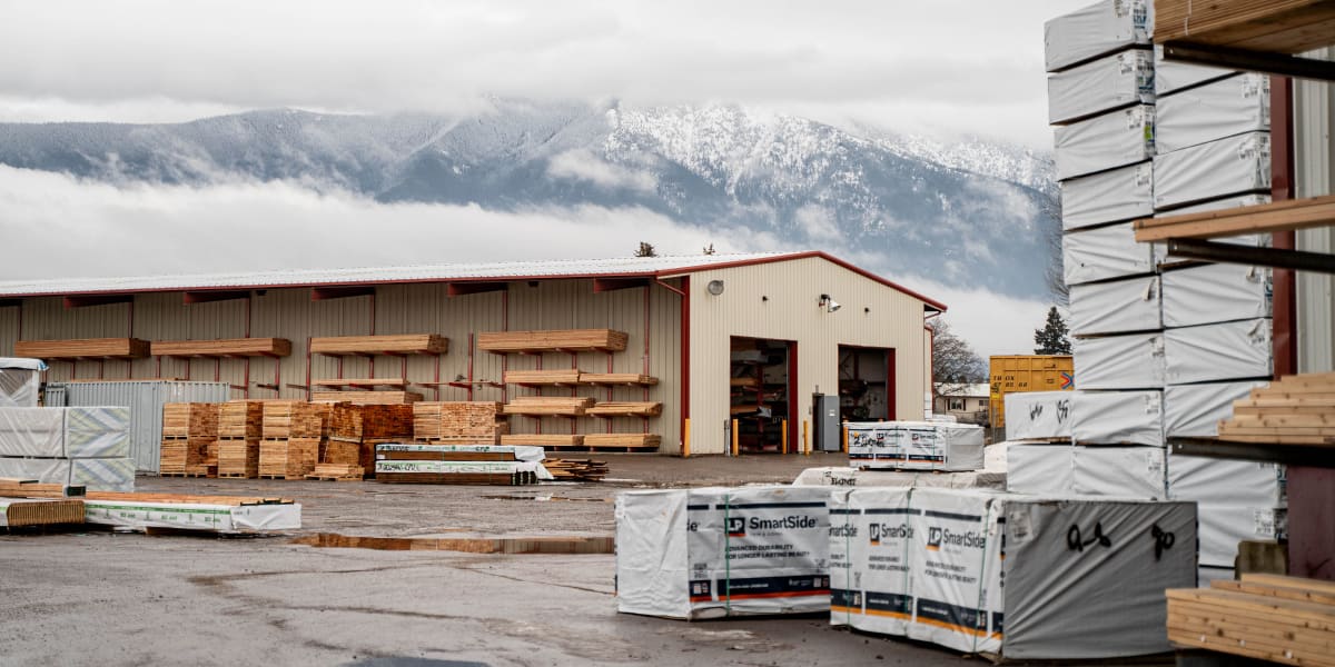 This image shows the lumber yard and warehouse facility of a Western Building Center location with snow-capped mountains visi