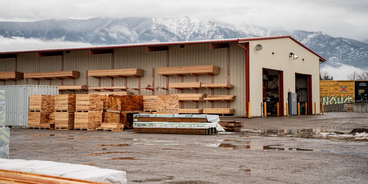 This image shows the exterior of a Western Building Center lumber yard facility with a large beige metal warehouse building f