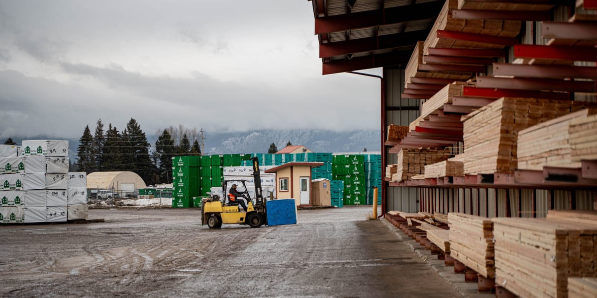 A lumber yard warehouse facility showing stacks of dimensional lumber organized on covered storage racks extending along the