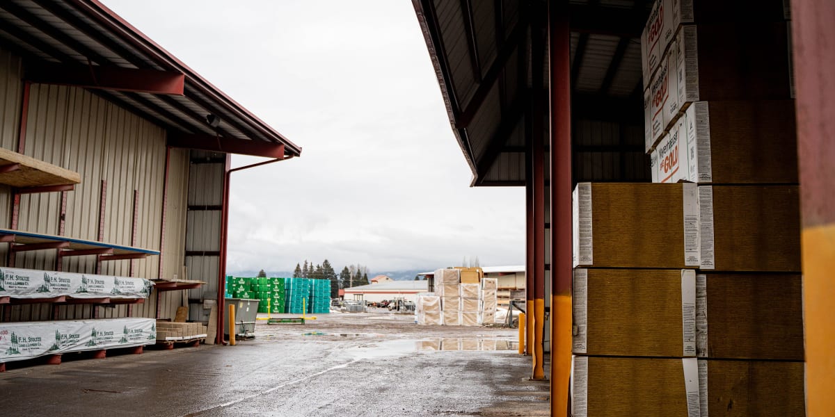 This image shows a covered warehouse loading area at a building supply center with stacked building materials organized under