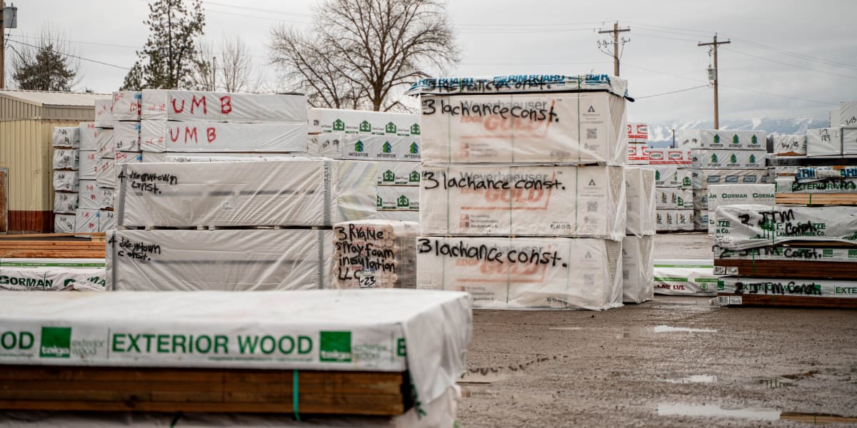 This image shows a lumber yard storage area with stacks of wrapped building materials and lumber packages