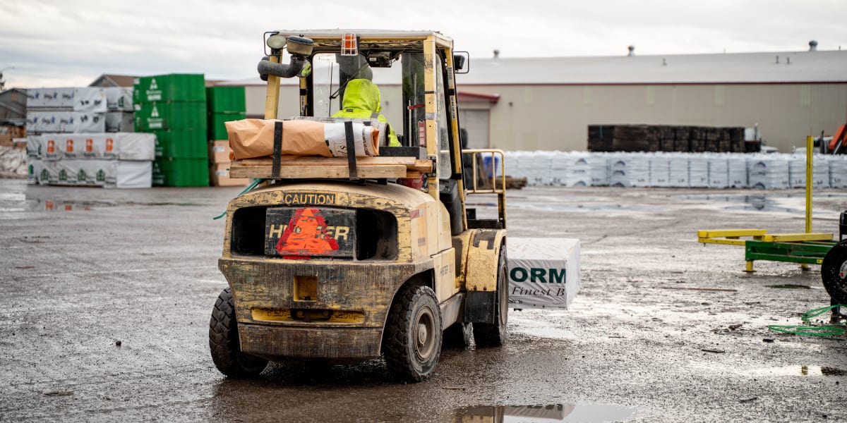 A Hyster forklift operates in a lumber yard, carrying building materials on wooden pallets