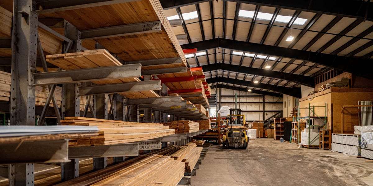 Interior view of a large warehouse lumber yard showing extensive metal cantilever racking systems storing dimensional lumber