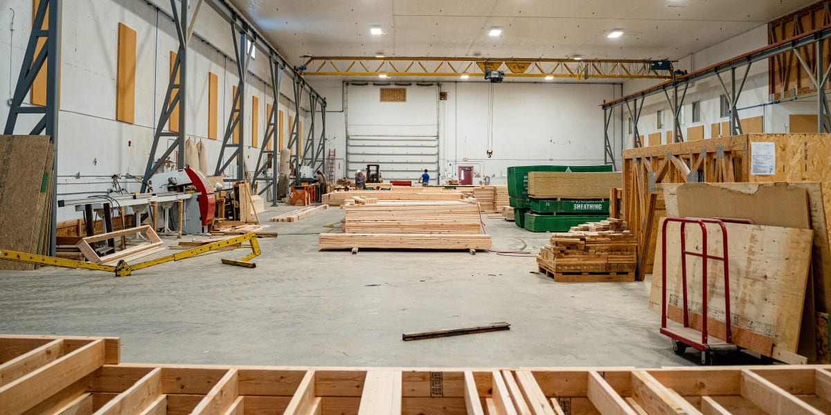 Interior view of a large industrial truss manufacturing facility with high ceilings, overhead crane system, and concrete floo