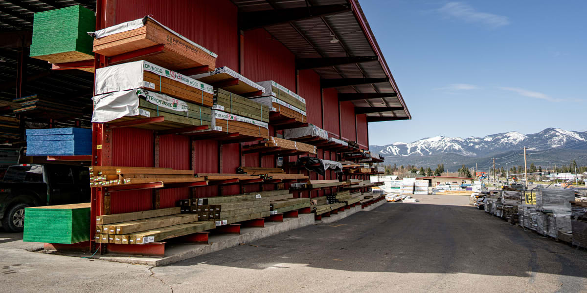 A lumber yard storage area showing extensive organized lumber inventory stored on cantilever racks under a covered outdoor sh