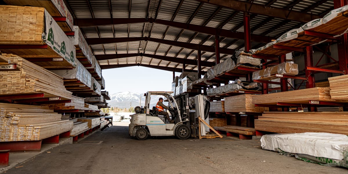A covered lumber warehouse showing organized storage of dimensional lumber and building materials on red cantilever racks