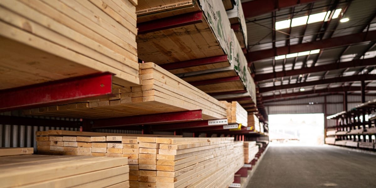 Interior view of a lumber warehouse showing extensive stacks of dimensional lumber organized on red metal cantilever racking
