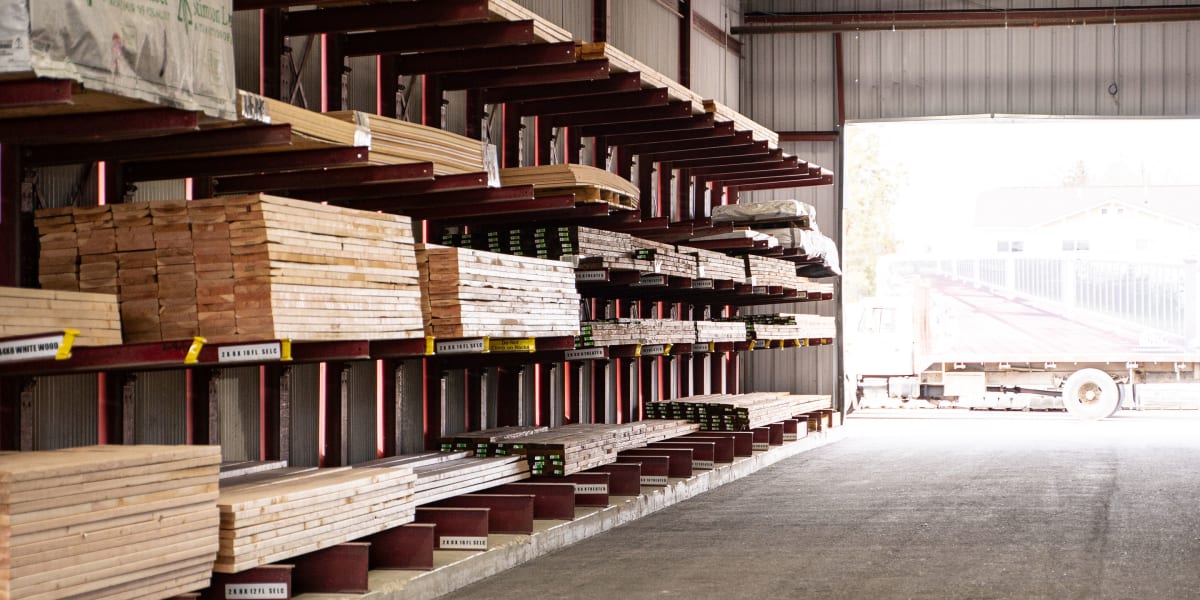 Interior view of a lumber warehouse showing organized cantilever racking systems holding various dimensional lumber, plywood,