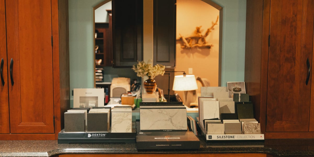A kitchen showroom display featuring multiple sample books and material swatches arranged on a dark granite countertop with r
