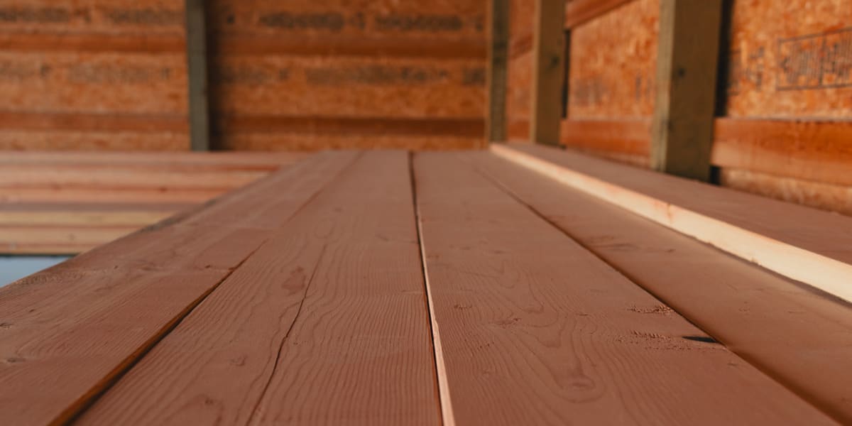 This image shows a close-up perspective of cedar or redwood deck planks from a low angle, creating a dramatic vanishing point