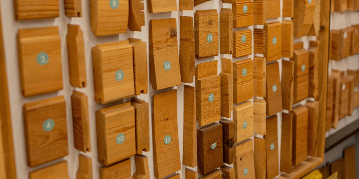 A detailed display of various wood species and finishes arranged in a grid pattern on a white wall, each sample numbered with