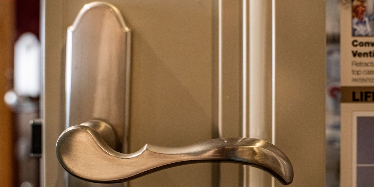 Close-up detail shot of a brushed nickel or satin chrome door handle with curved lever design mounted on what appears to be a