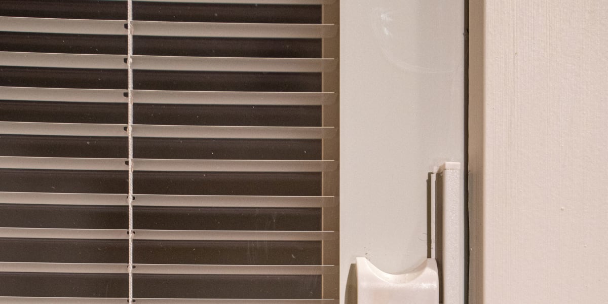 Close-up view of a white sliding patio door handle and frame detail with horizontal window blinds visible in the background