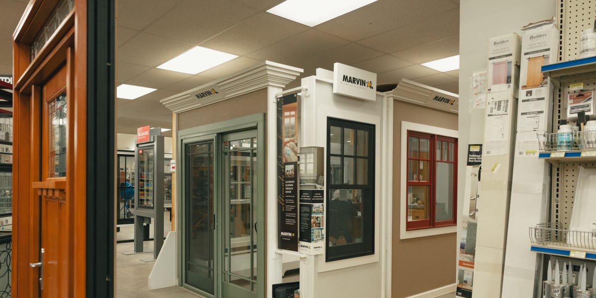 Interior showroom display featuring multiple Marvin window and door units mounted in white display walls with crown molding