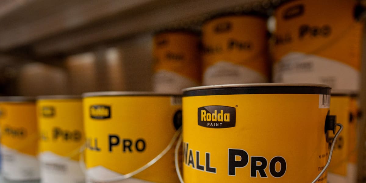 Paint cans are lined up on a store shelf, with Rodda Paint 'All Pro' interior primer cans prominently displayed in the foregr