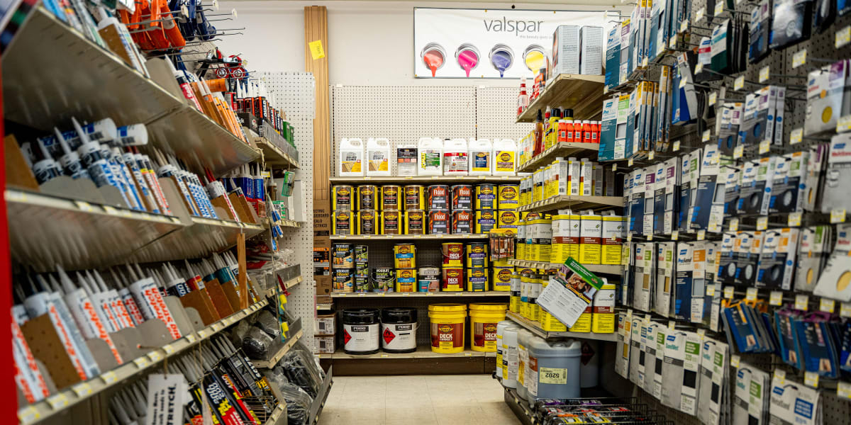 Interior paint aisle showing extensive shelving with numerous paint cans, stains, and wood finishes organized on both sides