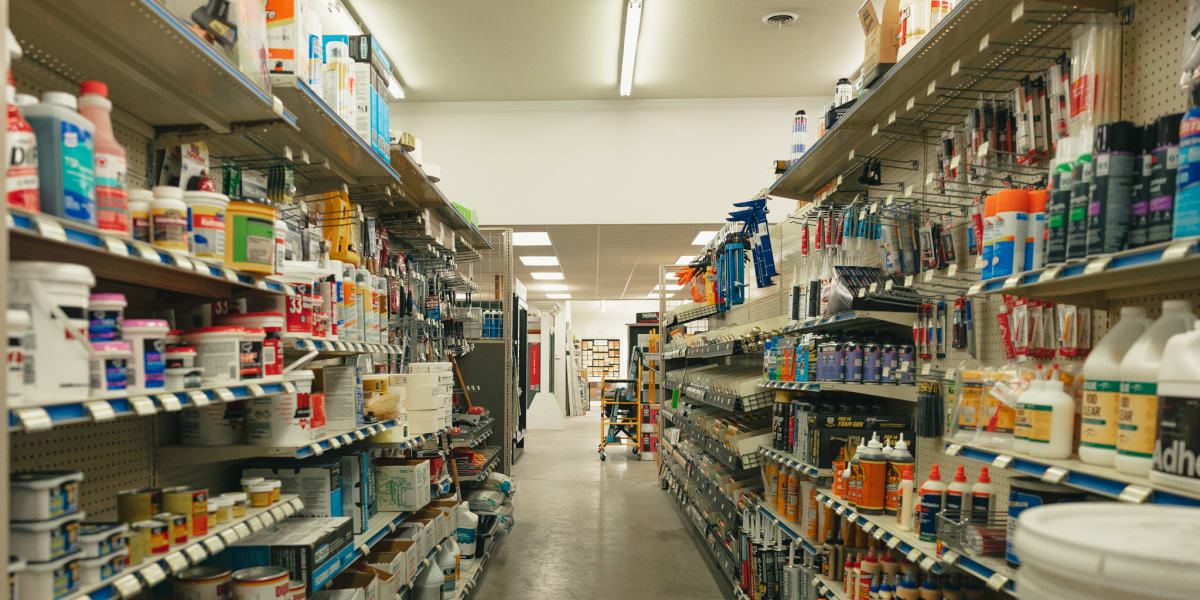 Interior view of a paint department aisle showing extensive shelving stocked with paint cans, stains, primers, and painting s