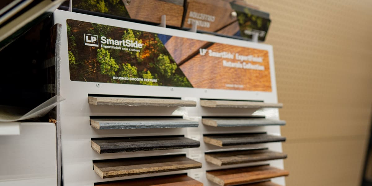 A siding sample display rack showing LP SmartSide products with multiple wood-textured samples in various colors and finishes