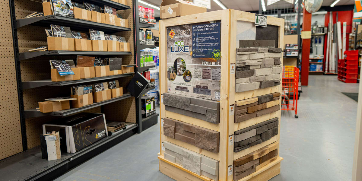 Interior store aisle showing an ADORN EcoLuxe Premier Series stone veneer display unit with multiple samples of manufactured