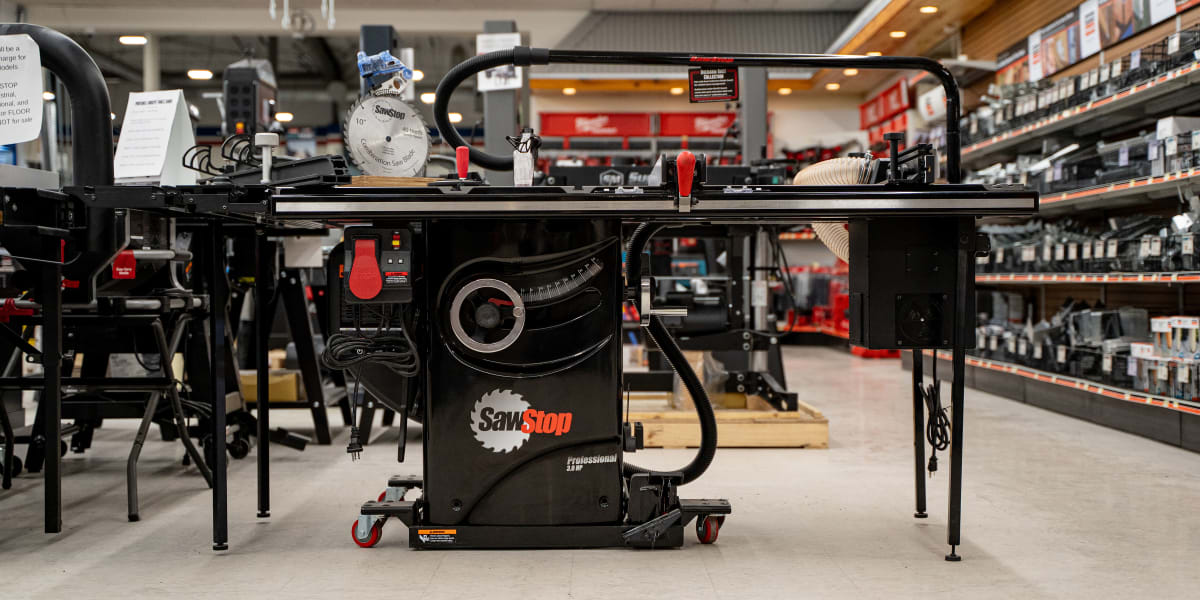 A SawStop Professional table saw with dust collection system and outfeed table is prominently displayed in a hardware store's