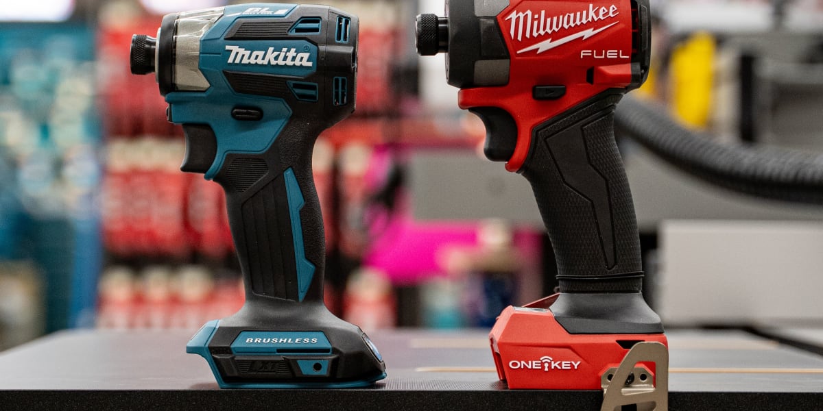 Two cordless impact drivers are displayed side by side on a black metal shelf in what appears to be a hardware store