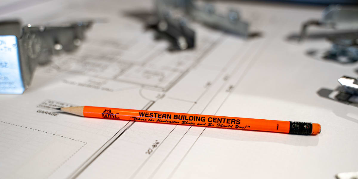 A close-up view of an orange Western Building Centers pencil laying on architectural blueprints or construction drawings
