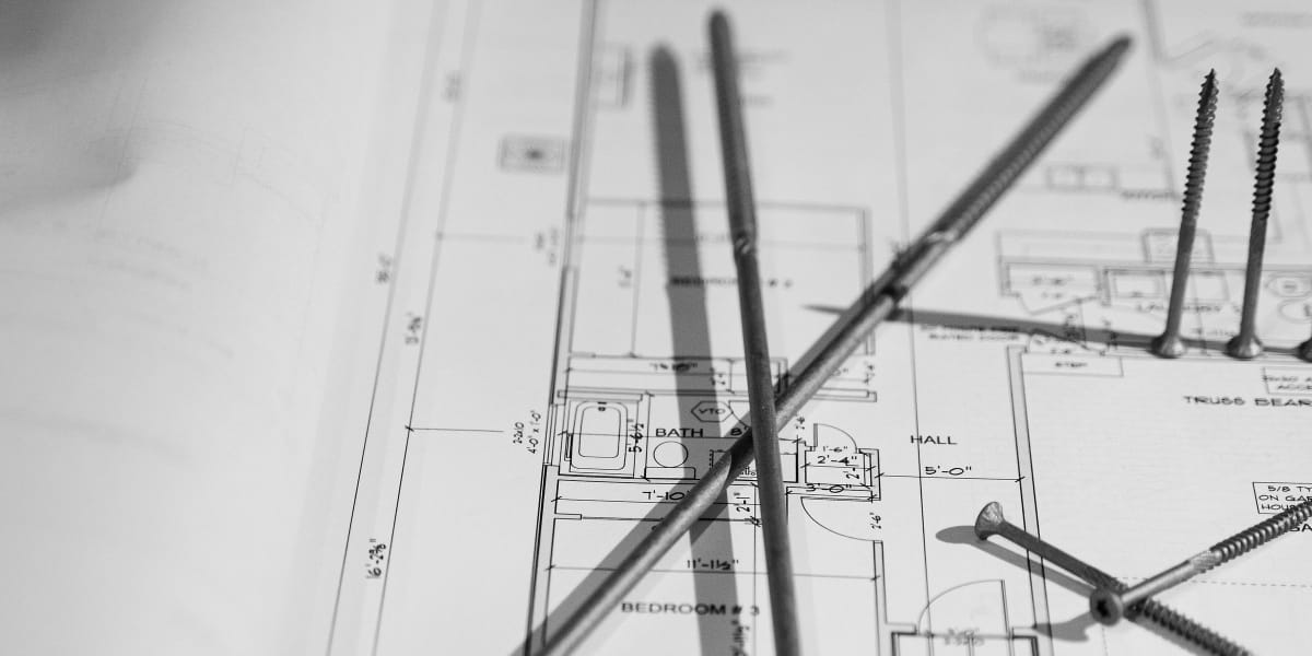 Black and white photograph showing architectural drawing tools including a compass, pencils, and measuring instruments laid o
