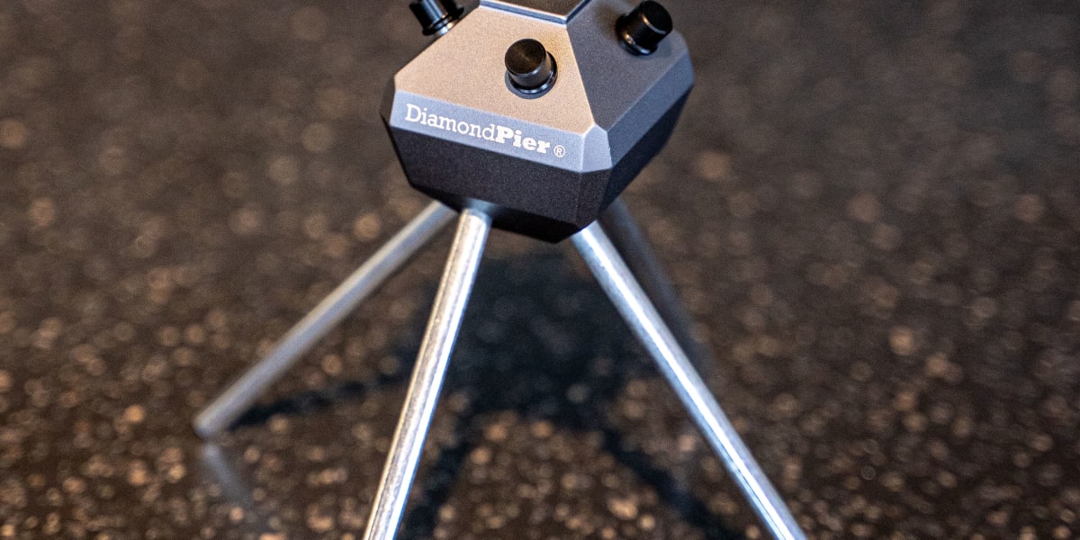 A DiamondPier ground screw foundation system tool mounted on a small tripod stand, photographed on an asphalt surface