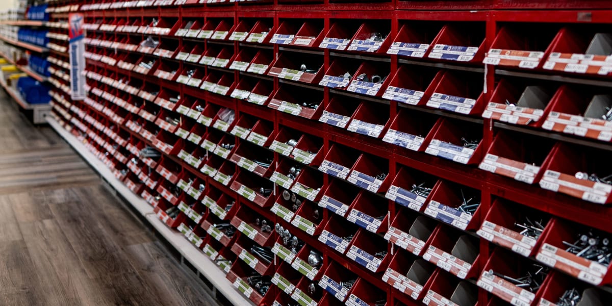An extensive hardware aisle displaying a well-organized wall of red storage bins and compartments filled with small hardware