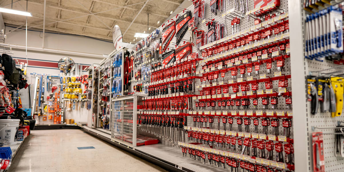 Interior view of a hardware store's tool aisle showing extensive displays of hand tools mounted on pegboard walls