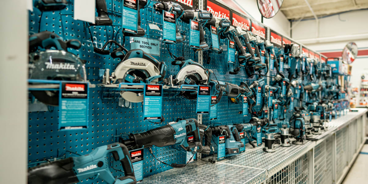 A well-organized Makita power tools display section in a hardware store, featuring numerous cordless tools mounted on blue pe